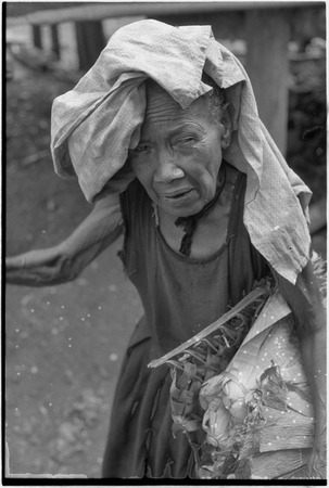 Mortuary ceremony: elderly woman, Bomtavau, wearing head cloth carries banana leaf bundle (wealth item) in basket
