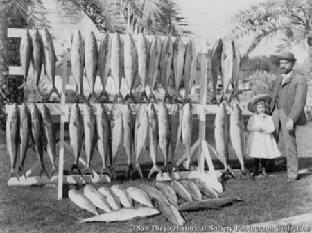 Man and young girl standing beside catch of fish on display