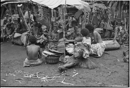 Mortuary ceremony, Omarakana: woman (center) holds stack of banana leaf bundles, other bundles in baskets