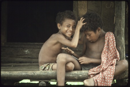 Boys play on house veranda, one picks nits from the other&#39;s hair