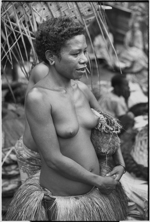 Mortuary ceremony, Omarakana: woman in fiber skirt holds small basket