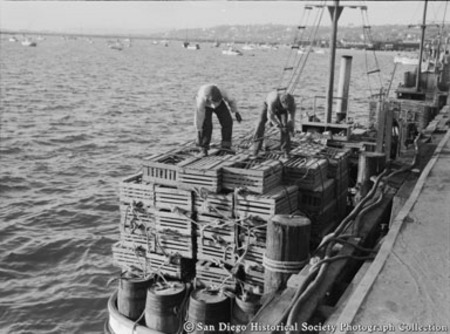 Two men on docked boat securing stack of lobster traps
