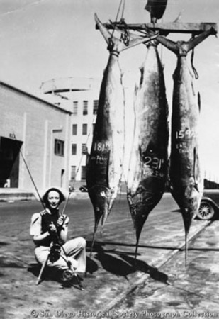 Woman holding two fishing rods posing with display of three marlins
