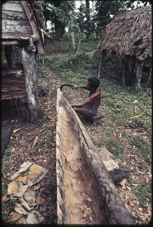 Canoe-building: man uses an adze to hollow out a log, creating base for large canoe