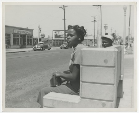Young African American woman and man seated at bus stop, San Diego