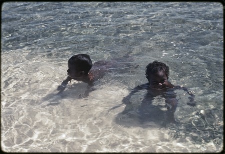 Children play in shallow clear water at a beach on Kiriwina near Kaibola village
