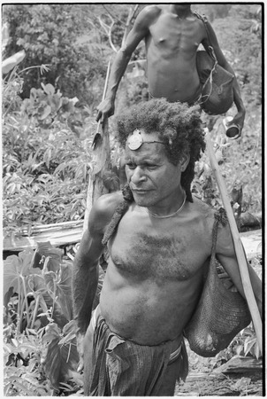 Gardening: luluai and another man in garden carry netbags (bilum) full of food