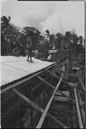 House-building: men frame a building and attach corrugated metal roofing