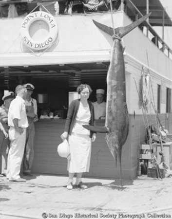 Woman posing with marlin hanging on display, Point Loma
