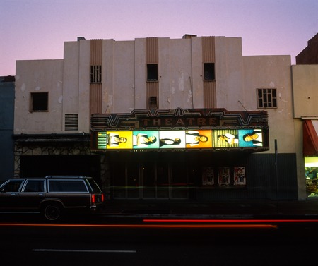 Awasinake (On the Other Side): theatre facade with marquee photographs at dusk