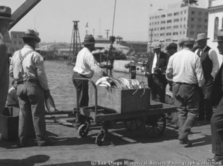 Dockworkers and crate of fish on dolly, Van Camp Sea Food Company dock