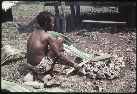 Woman heats and flattens pandanus leaf over a fire, softening it for use in weaving