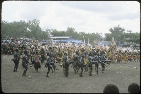 Port Moresby show: dancers with blackened skins, carry drums and spears, large banner in background