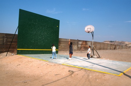 The Rules of the Game: ball court and border fence with children playing