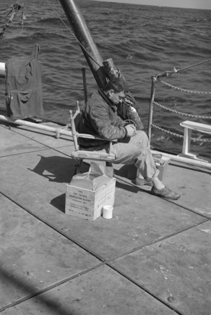 [Man seated on deck of R/V Spencer F. Baird with a box of TNT for seismic profiling]
