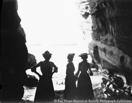 Three women standing on beach between rock formations, Encinitas