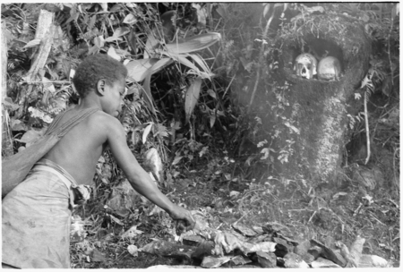 Young boy tending fire with skulls in background.