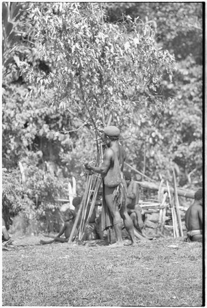 Men on grounds of government rest house in Tsembaga, bows and arrows propped beside them