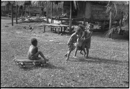 Children playing, pulling boy on a makeshift cart in Tukwaukwa village, Kiriwina