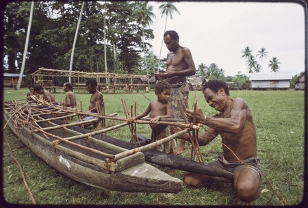 Canoe-building: men attach an outrigger float to a canoe, young child observes