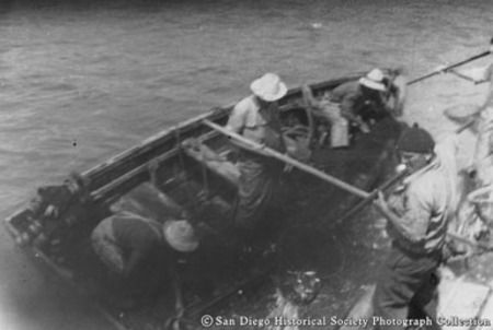 Fishermen on net skiff scooping bait from net to fill bait tank on tuna boat Chicken of the Sea
