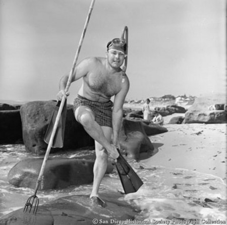 Snorkeler with fishing spear on rocky beach putting on flippers