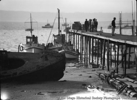 Docked fishing boats, fishermen standing on pier