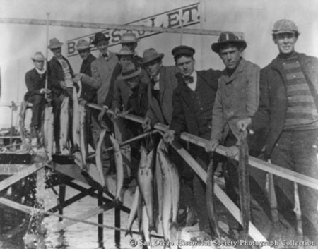 Group of men lined up on dock holding catch of fish