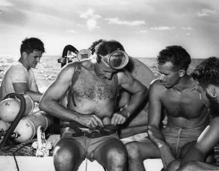 Divers, including Walter Munk (securing belt) and Willard Bascom (to right of Munk), work from a motor launch at Alexa Ban...