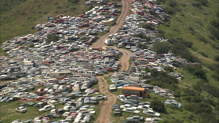 Osmosis and Excess: film still depicting Tijuana hillside covered in junk cars