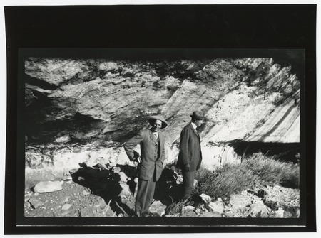 Ed Fletcher and unidentified companion, standing near rock cliff overhang