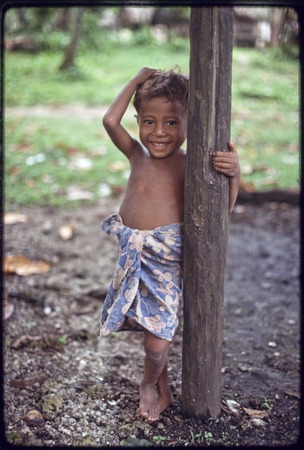 Young boy leans on a post and smiles