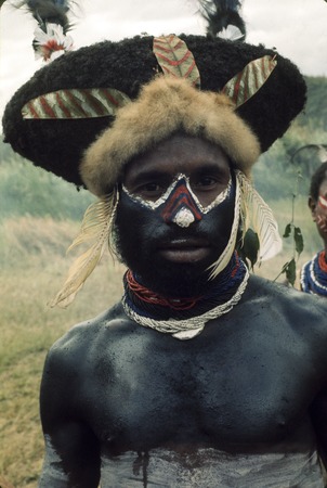 A young man in ceremonial garb, blackened face and body, wig with feathers and marsupial fur band