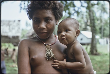 Adolescent girl, wearing shell necklace and dabs of betel nut paste on her cheeks, holding a baby