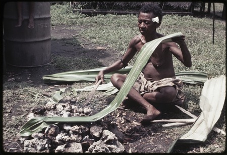 Woman heats and flattens pandanus leaf over a fire, softening it for use in weaving