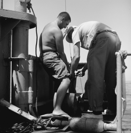 [Two men deploying the Peterson grab sampler from bucket on deck of R/V Spencer F. Baird]