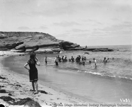 Girl in bathing suit looking back at people in ocean surf at La Jolla Cove