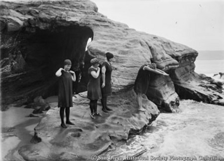 Three young women in bathing suits preparing to dive off rock formation into ocean