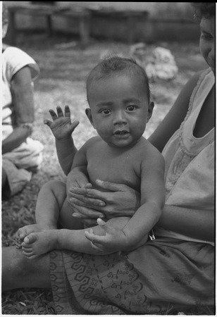Baby waving to the camera, sitting on woman&#39;s lap