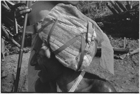 Man wears fabric and ribbon headdress with kinship chart pinned to it