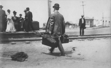 Unidentified man showed here carrying suitcases and golf clubs after arriving on the train at the La Jolla Railway Station...