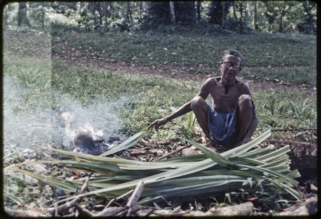 Bomtavau heats a pandanus leaf, preparing material for weaving