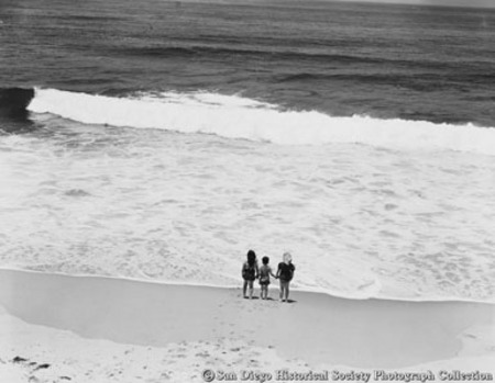 Three children holding hands on San Diego beach looking at ocean