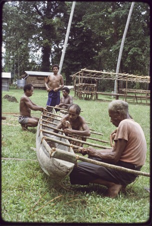 Canoe-building: men fasten outrigger supports to a canoe, using lengths of vine
