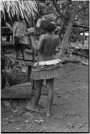 Adolescent girl, wearing short fiber skirt, Edwin Hutchins (in background) holding pen and notebook