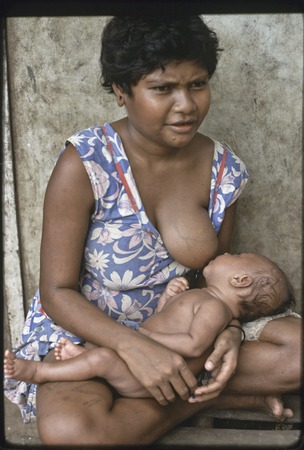 Mother breastfeeds infant on house veranda