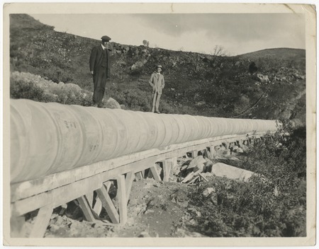 Men standing on trestle-supported steel flume