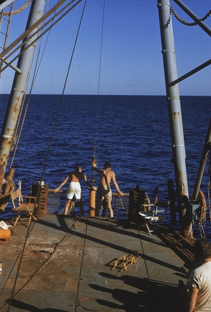 An unidentified man and Arthur Eugene Maxwell (in white shorts) lowering instrument at the stern of the ship. Maxwell help...