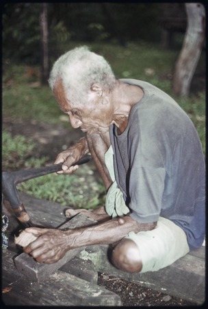 Carving: older man uses an adze with metal blade to shape a piece of wood
