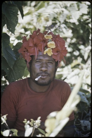 Man wears red hibiscus flowers in hair and smokes a cigarette